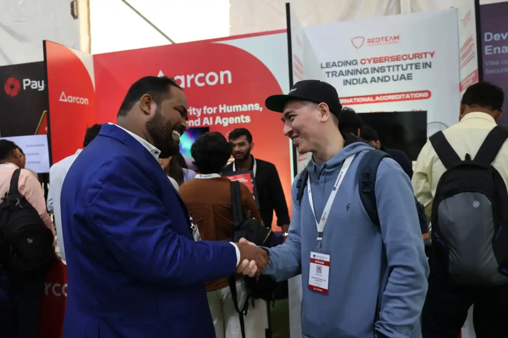 Attendees shaking hands at the RedTeam Hacker Academy booth during the IdentityShield Summit 2026 cybersecurity event in Pune, showcasing cybersecurity training and industry networking.