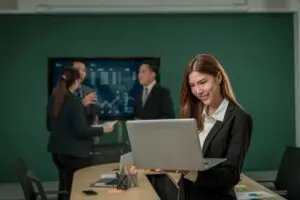 “Professionals in an office environment focusing on cybersecurity training, with a businesswoman working on a laptop while colleagues discuss data security, representing the importance of upskilling in cyber defense.”